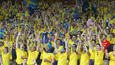Svenska fotbollssupportrar står på en läktare och hejar på det svenska landslaget.