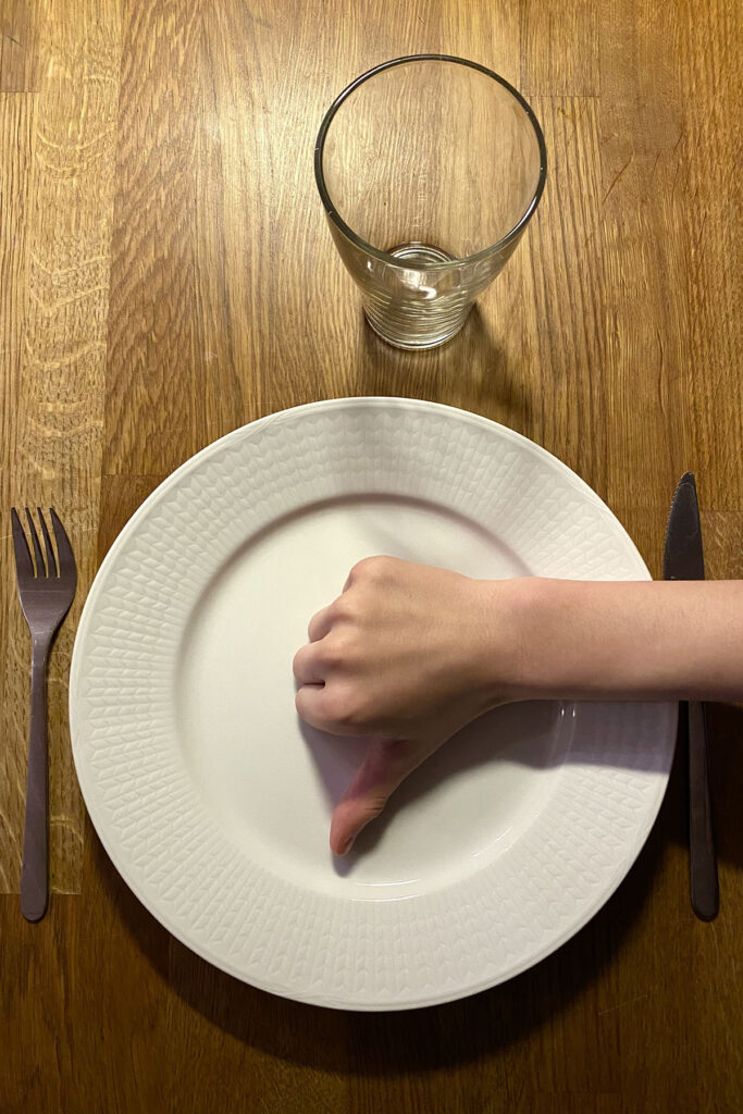 En tom tallrik med en hand på som gör tummen ner.